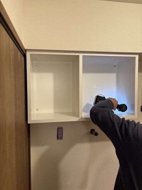 練馬区のH様邸では家具屋による吊戸の設置が行われていました。 74㎝の洗濯機パンを使うので、上部に75㎝幅のオープン棚収納を設けました。 簡単なオープン棚や既製品でも良さそうな場所にわざわざ造作家具を使ったのには理由があります。 もともとこちらのお宅は洗濯機の上にメッシュのオープン棚が1枚あり、そこにフェイスタオルを平置きしてたくさん積んでお使いでした。 というのも、H様は手を洗ったら都度新しいタオルを使う習慣があり（ですのでタオル掛けは必要ありませんでした）、タオルを沢山お使い、かつすぐに手に取れるようオープンな状態が良かったのです。 棚板ではタオルを積んだ時にずれて雑多に見えがちなこと、そしてそれまでは足元に置いて使われていた洗剤も置けるように、ハコ型が良いと思いました。 さらに梁下ということで寸法の制限もあり、わざわざ造作にしたわけです。 前もって伝えておいた形で造ってきてくれ、現場では取付けのみ。 あっという間に取付け完了、ついでと言ってはなんですが、隣のトイレの吊戸棚（こちらは既製品）も取付けしてもらいました。 ささやかな場所のささやかな工夫ですが、生活の中で満足感に大きな差があるのでは…と思っています。